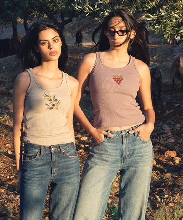 Two women standing outdoors in a natural setting, wearing tank tops and jeans.