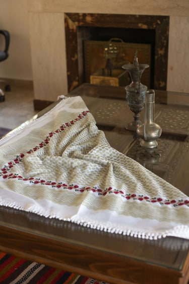 Handmade Olive Zaytoun Tatreez Keffiyeh displayed on a wooden table with traditional artifacts.